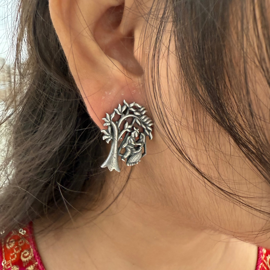 Close-up of a person wearing a silver tree-shaped earring with a red garment in the background.