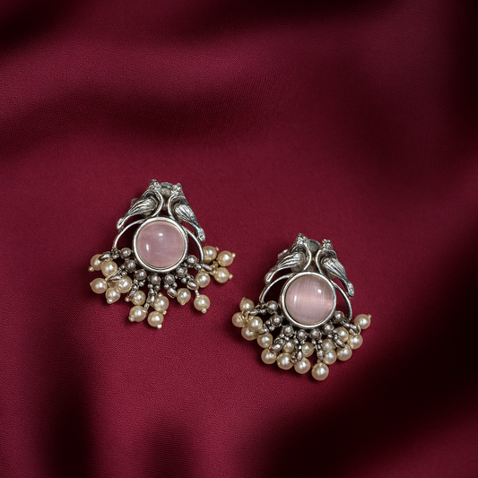 Pair of ornate earrings with pink stones and pearl-like beads on a red fabric background