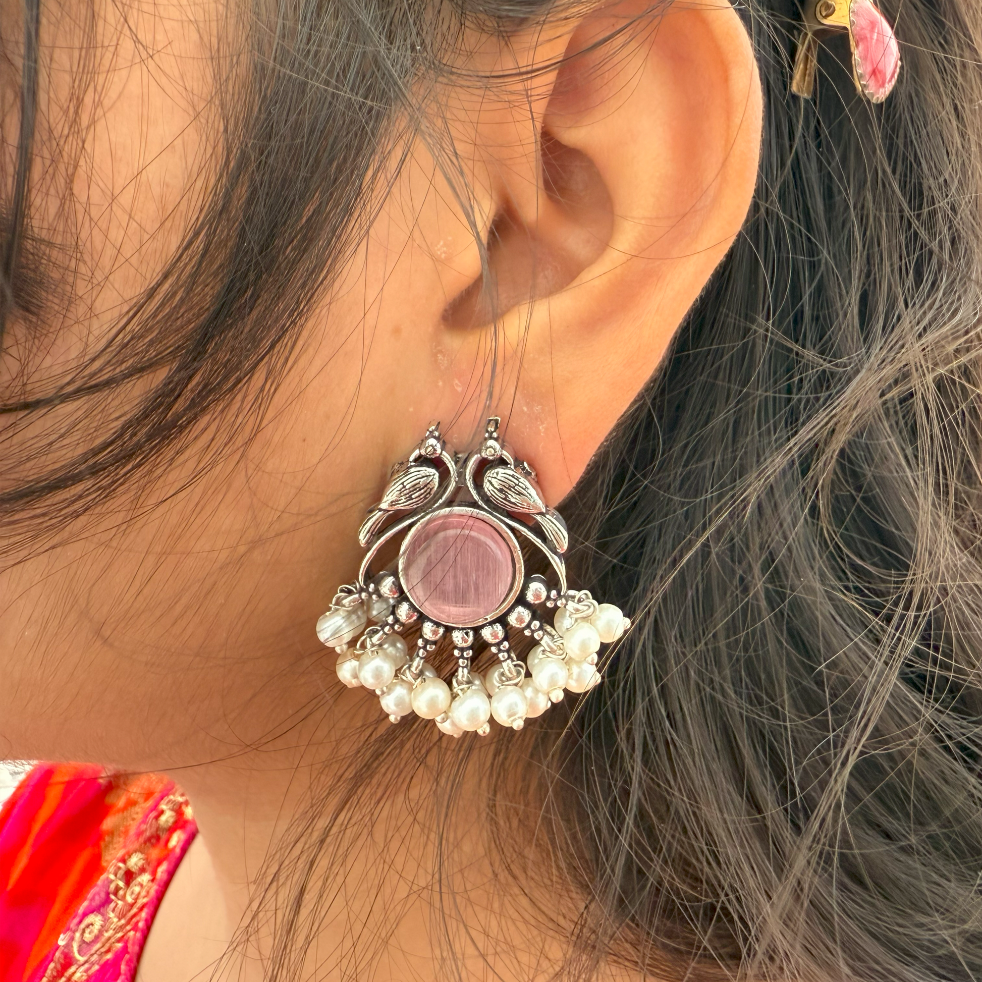 Close-up of an ornate earring with a pink center worn by a person with dark hair.