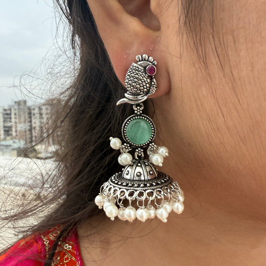 Close-up of an ornate earring with pearls and gemstones, worn by a person with a blurred background.