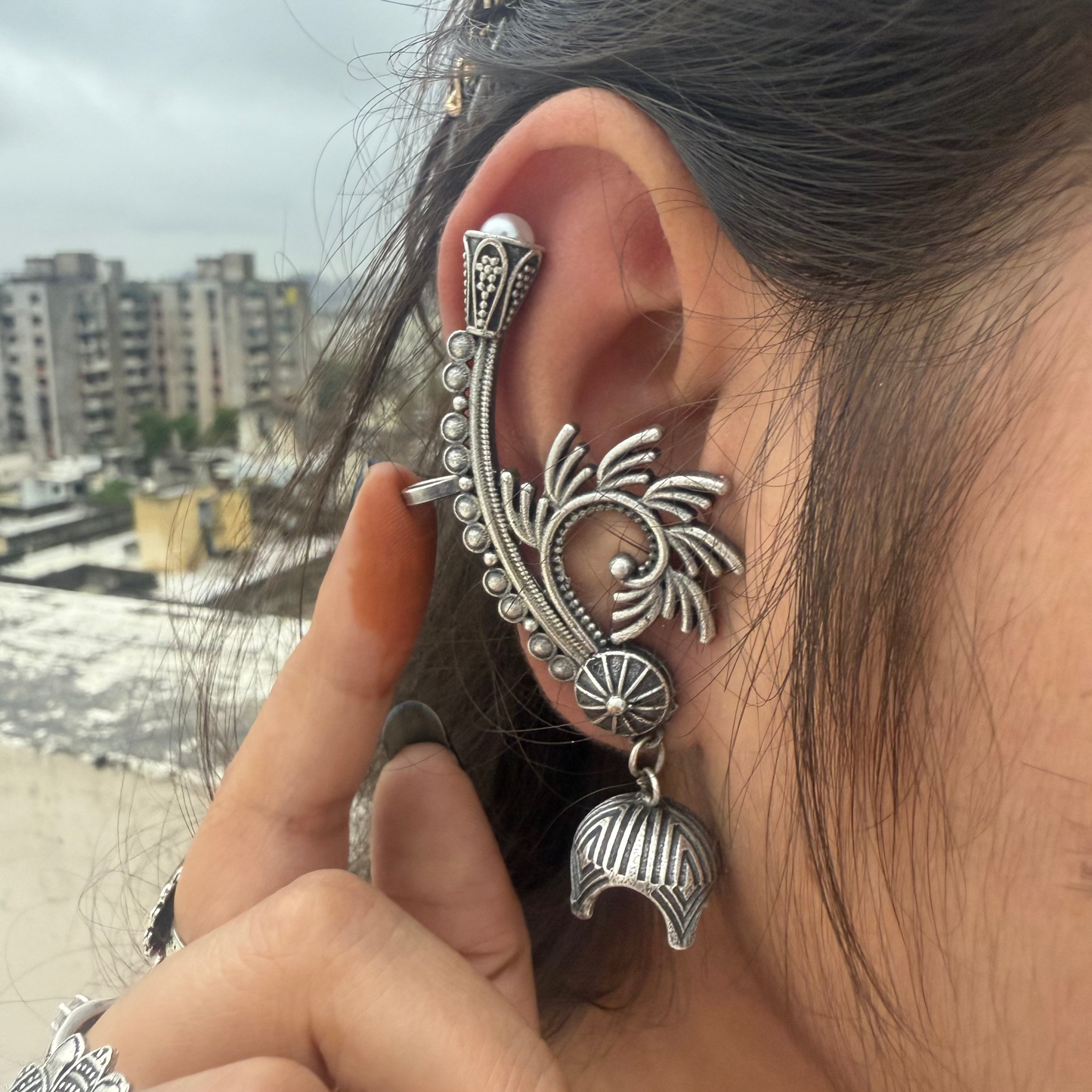Close-up of a person wearing an ornate silver earring with a cityscape in the background.