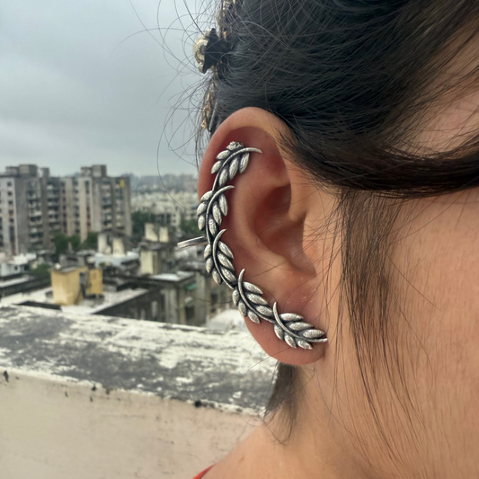 Person wearing a silver ear cuff with an urban landscape in the background