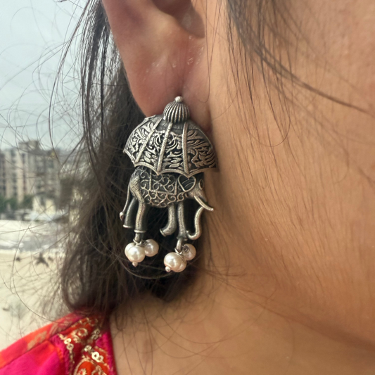 Close-up of a person wearing an ornate silver earring with pearl-like beads, outdoors.