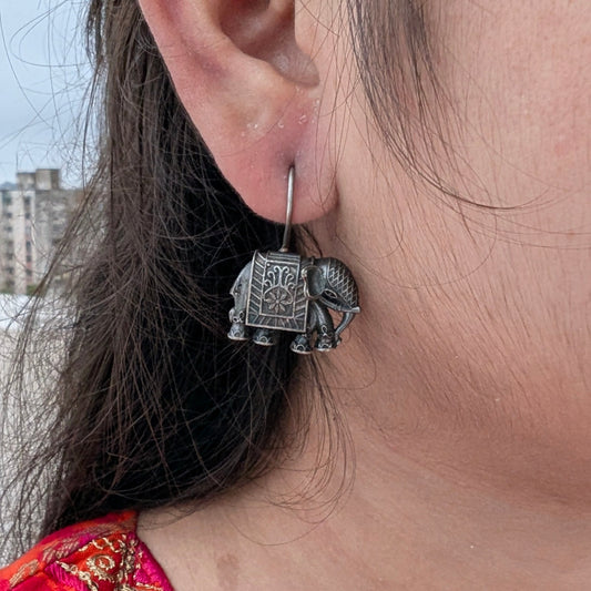 Close-up of a person wearing a silver elephant earring with a blurred background