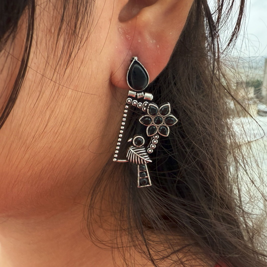 Close-up of an ornate silver earring with black stones worn by a person.