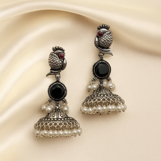 Ornate silver earrings with black and pearl details on a beige fabric background
